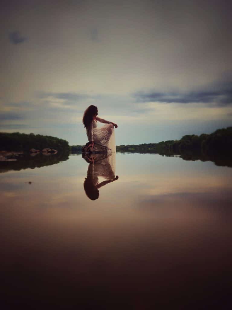 woman in white dress sitting meditating by the water.