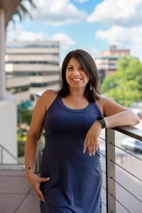 Wendie Veloz Social Impact Strategist pictured in blue dress standing against a railing
