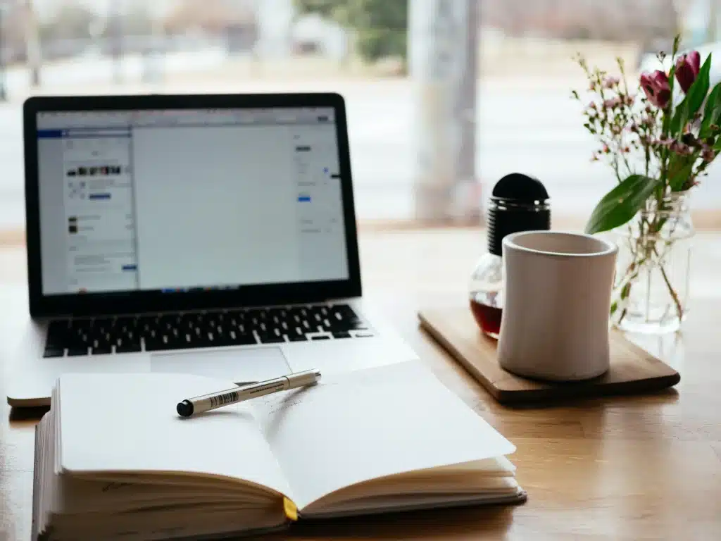 Image of notebook with pencil and computer with coffee next to it. Idea 2 Impact Grant Writing Course helps you write a strong grant narrative.